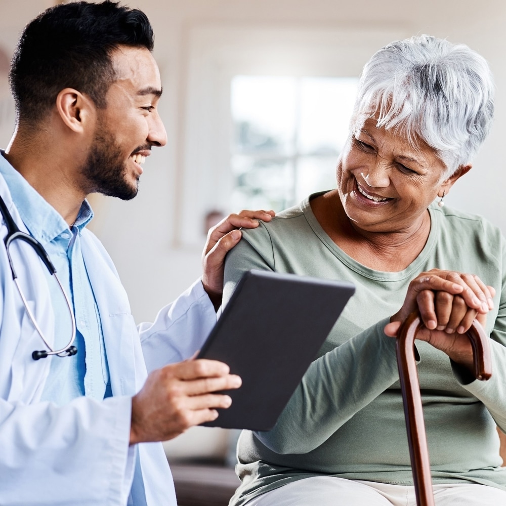 A doctor has a conversation with a patient. They are in his office and both smiling.